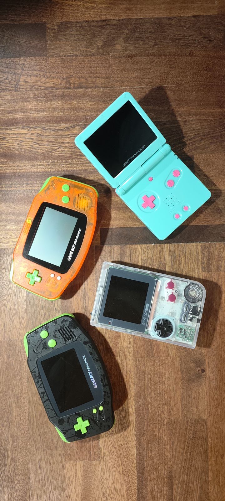 Four modded Game Boys: an orange GBA, a black and lime GBA, a mint SP and a clear Pocket